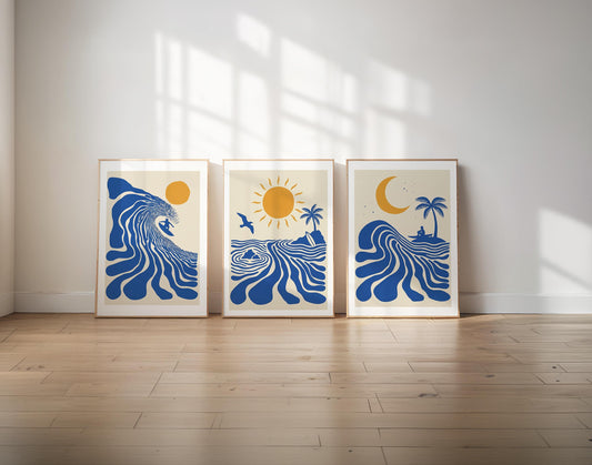 Three framed art prints with blue ocean wave and sun motifs are displayed side-by-side on a light wood floor against a white wall with window shadow projections.